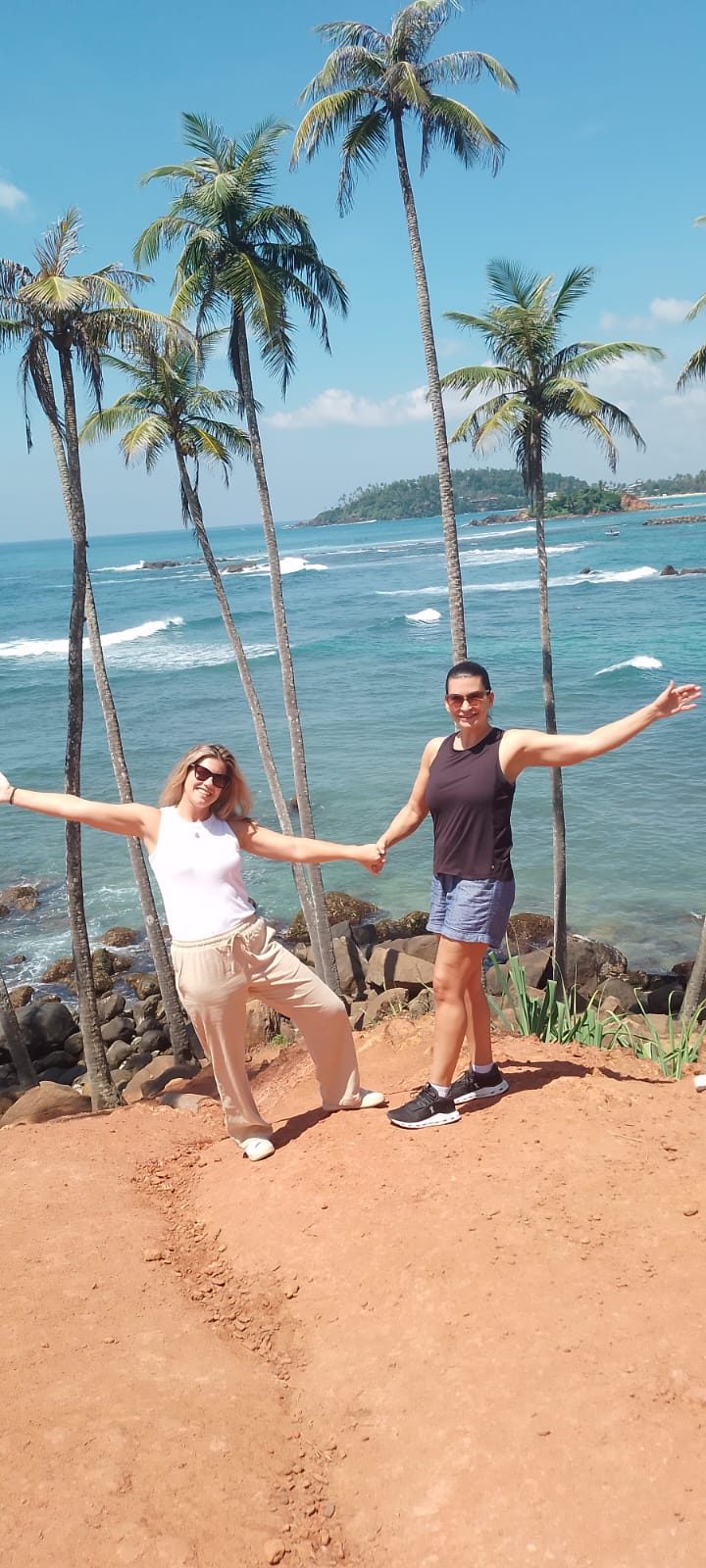 Two travellers with arms outstretched on Coconut Tree Hill above a turquoise bay