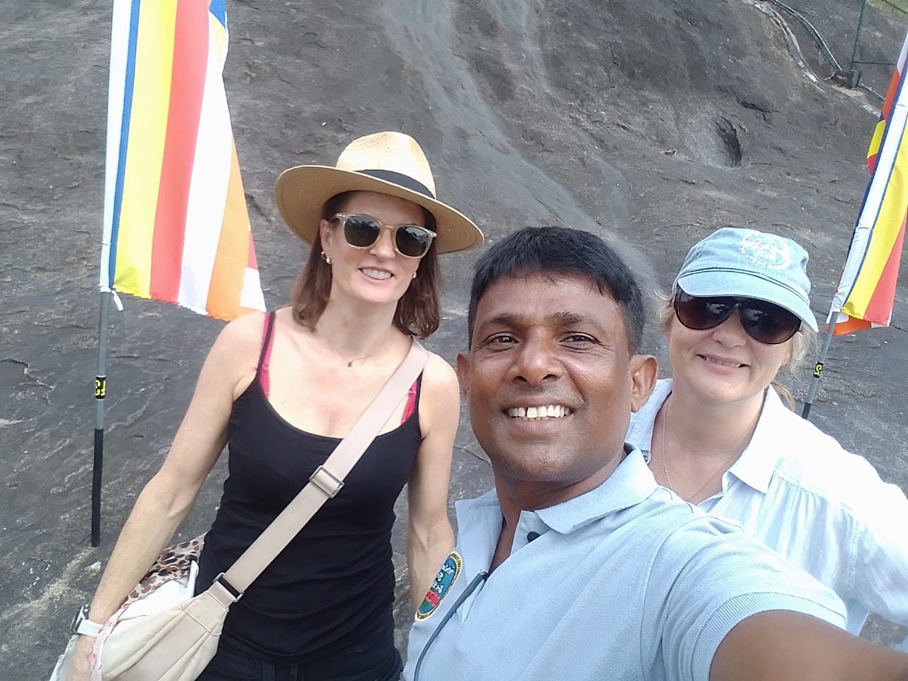 Chin with two guests beside Buddhist flags on a rock temple
